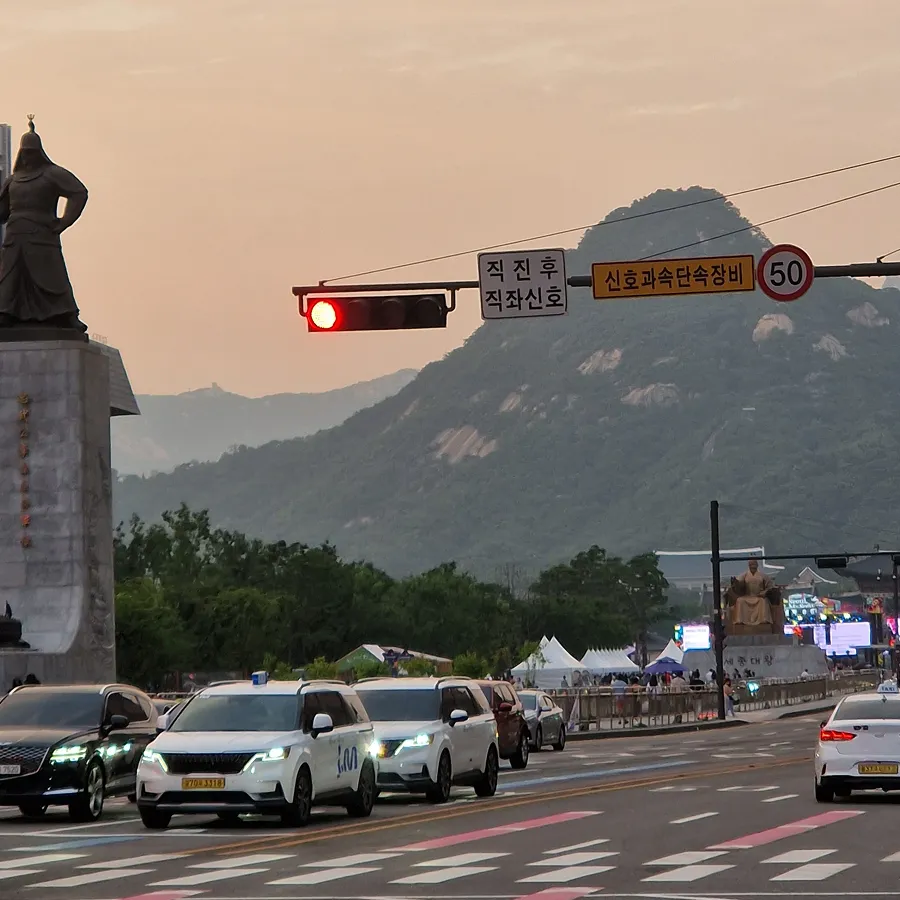 Traffic passing Gwanghwamun Square in Seoul with Bugaksan mountain in the background.